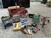 Photo of all items including metal model tractor, military Jeep model, green glass insulator, brass number one paperweight, various pocket utensils, vintage razor, military cards, and Audiphone in box.