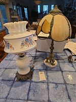 Photo showing both vintage lamps together on a blue tiled surface, including the white milk glass floral lamp and the slag glass lamp with broken panel