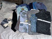 Wide view of all vintage mens shirts folded, assorted patterns and colors visible, with black necktie, cream bowtie, and white napkins at left.
