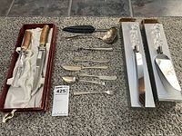 Overview shot of all vintage utensils including antler-handled carving set, crystal-handled cake servers, metal ladle, small forks and knives, and metal tray.