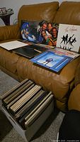 Box containing over 50 vinyl LPs with several album jackets displayed on a sofa