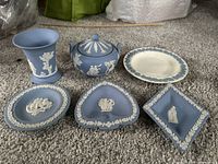 Top-down view of the full collection showing the Jasperware vase, lidded candy dish, three various shaped trinket dishes, one larger Wedgwood dish, all in blue with white classical relief decorations.