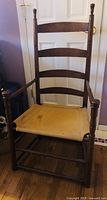 Front view of the wooden ladder back chair showing the four horizontal slats and woven seat with some stains.