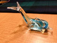 Blue and green accented clear Murano style glass dolphin figurine on a wooden surface, profile view