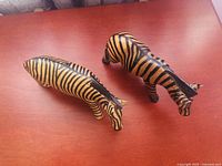 Top-down view of two hand carved and painted zebra figurines placed on wooden surface.
