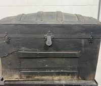 Front view of the antique humpback trunk showing black exterior with metal hardware and damage to one corner