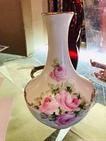 Side-angle view of white porcelain eau de toilette bottle with hand-painted pink and purple roses, gold gild trim on the neck and base.