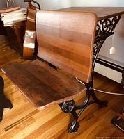 Side angle showing wood seat and cast iron leg with ornate detailing.