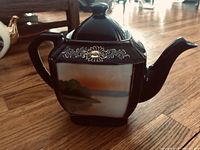 Blue ceramic tea pot showing hand-painted tranquil landscape and floral designs.