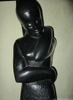 Front angled view of black cast metal woman sculpture showing crossed arms and textured surface details.
