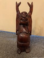 Full view of the hand-carved mahogany Buddha statue with arms raised, showing the full figure with rounded belly and joyous face.