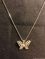 Front view of butterfly pendant on gold plated chain displayed on black velvet background.