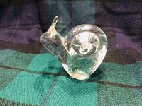 Clear crystal snail figurine approx 4 inches high on dark green and black cloth.