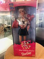 Front view of the special edition Walt Disney World Barbie doll inside unopened box. Doll wears silver and red jacket and holds red Mickey Mouse balloons.