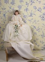Full view of the Effanbee Princess Diana doll seated, showing long flowing satin wedding dress with extended train and bouquet, against floral wallpaper background.