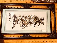 Photo of framed embroidered horse artwork with ornate dark wood frame and light blue mat. Five horses in motion embroidered in the center, with calligraphy details.