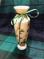 Full view of the Lefton bud vase 12 inch tall with green shamrock illustrations and green ribbon tied around the neck.
