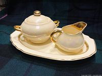 Photo showing the full sugar bowl with lid, creamer, and serving tray on a dark cloth background.