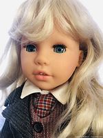 Close-up front face view of blonde haired Max Zapf doll wearing school girl outfit with blue eyes, white collar shirt, and plaid tie.
