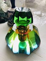 Front angle of the multi-faceted crystal perfume bottle showing the green crystal stopper and the vibrant light refracted colors of the crystal body.