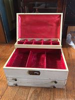 Photo of vintage cream jewelry box with red velvet lining showing top open compartment with six small sections and larger sections below.