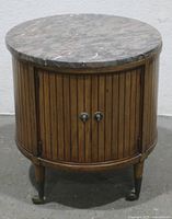 Front view of the vintage round barrel end table showing the removable grey marble top and vertical slat wooden cabinet doors with metal knobs.