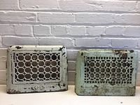 Two vintage metal air vents, one cream and one green, side by side on white surface with white brick background.