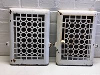 Front view of two white metal vertical vents with geometric cutouts, showing some paint chipping.