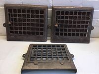 Three vintage metal air vents, two larger and one smaller, metal grid pattern, displayed on a surface.