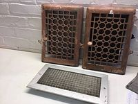 Front view of two vertical vents with decorative rusted grills and one smaller silver vent with grid grate on floor.