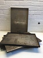 Full view of five metal printing trays stacked showing three sided raised edges