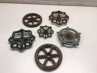 Six small old metal faucet crank wheels of different shapes and sizes on white surface showing wear and rust