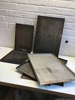 Six metal three-sided printing trays in two sizes stacked and arranged showing their shape and condition.