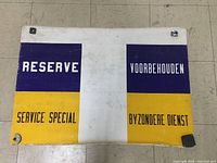 Full view of the vintage painted canvas sign showing color blocks and text in English and Dutch.