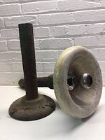 Photo of the rusted cast iron fountain post standing upright next to the marble basin body placed horizontally, showing the underside and the central metal knob.