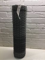 Full view of rolled chicken wire against a white brick wall, showing size and shape.