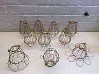 Overview of ten metal light bulb protector cages, showing round bases and wire protective structures.