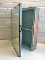 Medicine cabinet wooden frame with door open showing one shelf inside, viewed at angle, mirror on door visible.