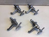 Set of four individual chrome-plated taps arranged on a flat surface, showing two hot and two cold water taps with cross handles and outlet spouts.