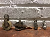 Four small pulleys arranged on wooden surface in front of white brick wall.