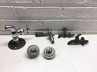 Wide view of all six items—two push button controls and four spigots on a white surface against a grey brick background.