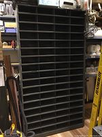 Full view of tall metal shelving unit with 68 cubby holes, dark grey color, standing upright in a storage or workshop area.