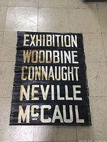 Full view of vintage painted canvas streetcar sign showing the destination names in bold cream letters on a black background.