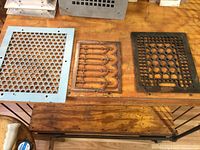 Three metal vent covers on wooden workbench showing all three different styles and conditions.
