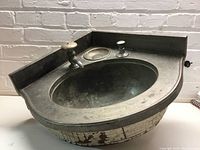 Overall view of the vintage metal and wood corner sink showing the basin, faucet, and soap holder, with noticeable aging and patina on the metal and chipping paint on the wood base.