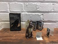 Front view of Bigwig figurine, original box and pamphlets laid out behind on wooden table with white brick wall background.