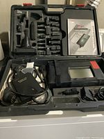 Open kit case showing diagnostic tool in leather sleeve, cables, connectors, and user manual