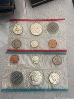 Two original sealed proof coin sets from 1963, one with a red trimmed holder labeled Denver Mint, the other with a blue trimmed holder labeled Philadelphia Mint.