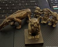 Group shot of all three miniature bronze figures, showing two monkeys and one dinosaur on a dark surface