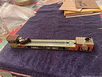 Full view of the Arnold tin litho wind-up toy train on the track showing the base with lithographed vehicle art and the miniature steam locomotive with attached track section on a fabric surface.